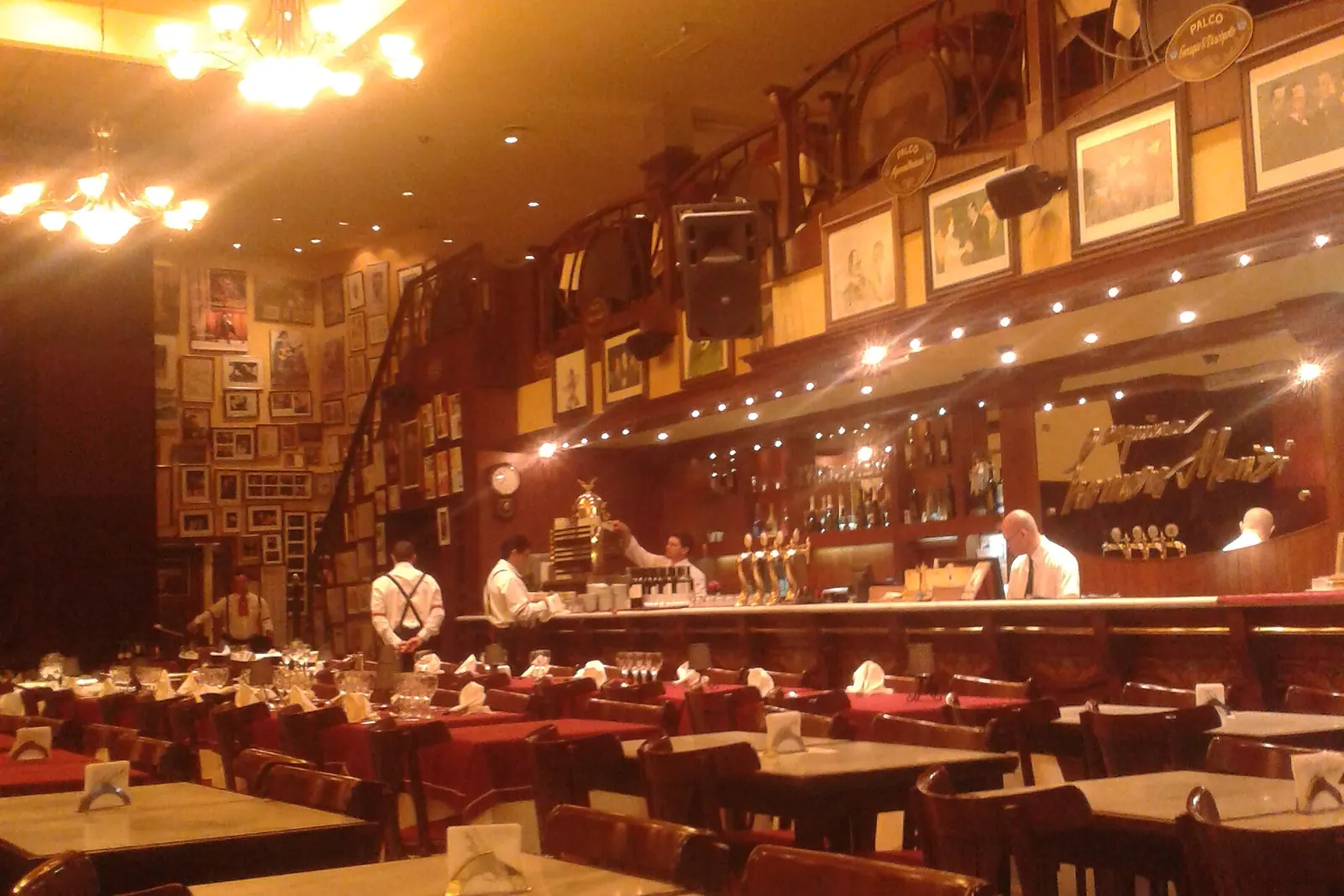 La sala da pranzo dell'Esquina Homero Manzi prima del servizio, con tavoli dal piano in marmo, tovaglie rosse, una galleria superiore di palchi adorni di quadri incorniciati e un lungo bancone