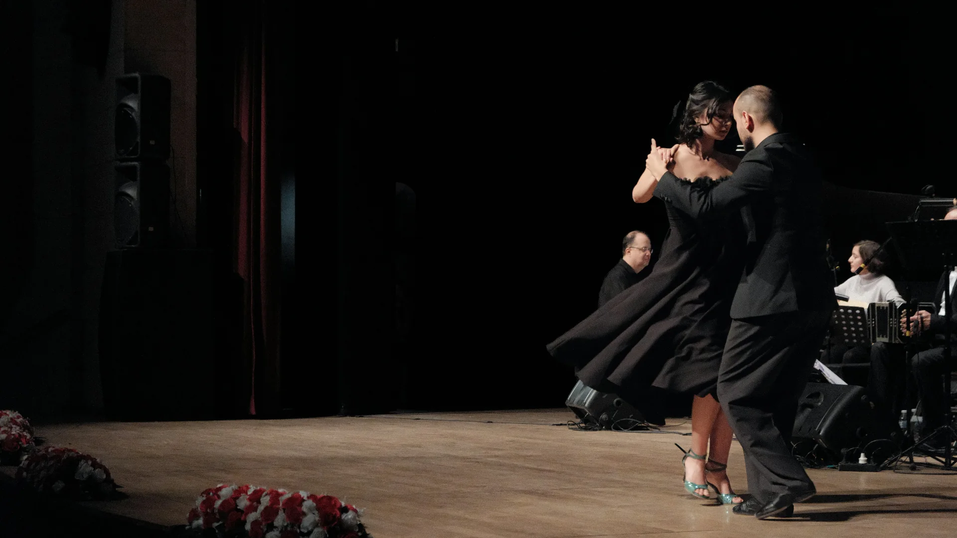 Una coppia di ballerini di tango in nero che si esibisce su un palco di legno accanto a un ensemble dal vivo con bandoneón, fotografata ad Ankara e non all'Esquina Homero Manzi