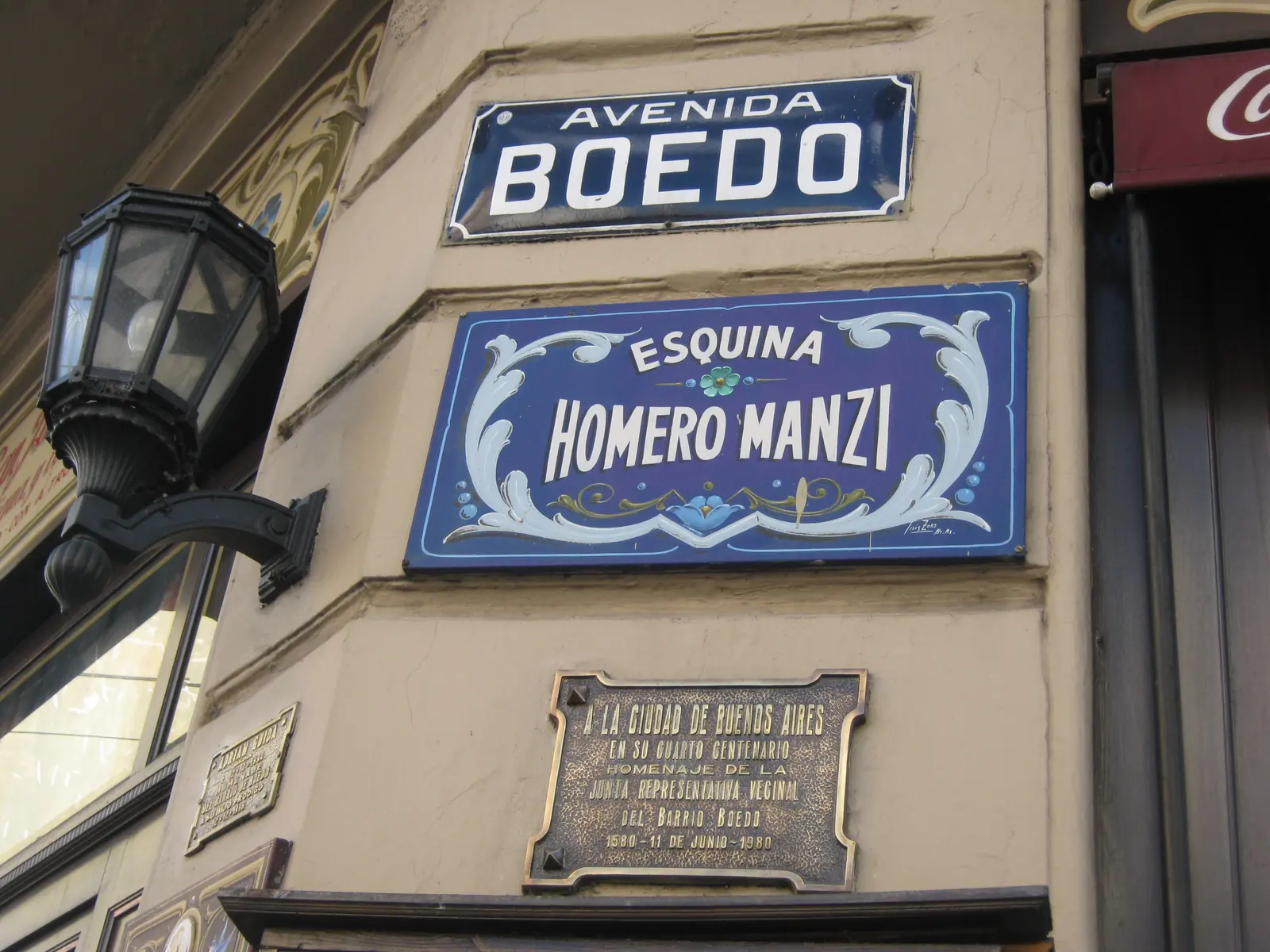 L'insegna d'angolo dipinta di blu con la scritta Esquina Homero Manzi sotto il cartello stradale di Avenida Boedo, con un lampione in ferro accanto